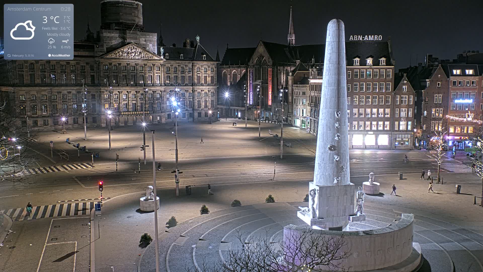 A mostly cloudy night scene shows a large, empty city square with a tall monument at its center, surrounded by historical-looking buildings and streetlights.