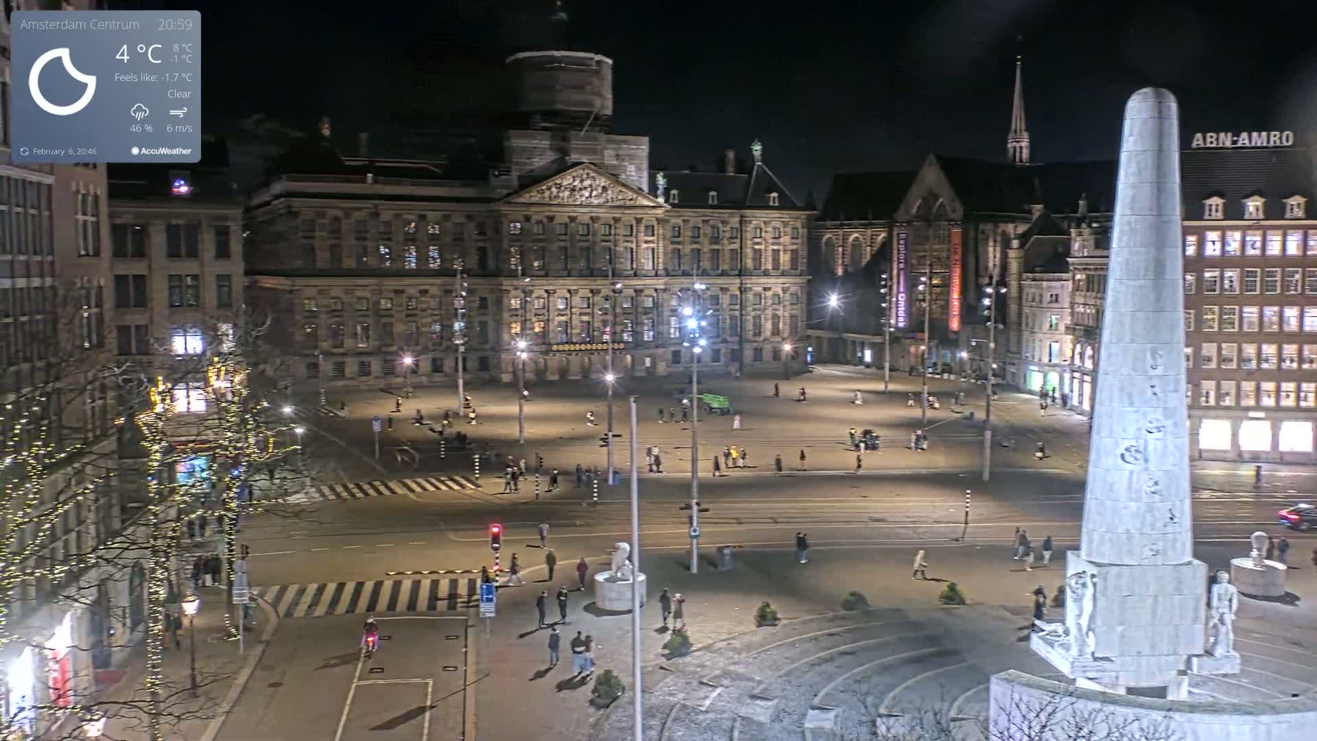 A nighttime, clear view of a large city square with a palace, a monument, and several buildings, sparsely populated with people.
