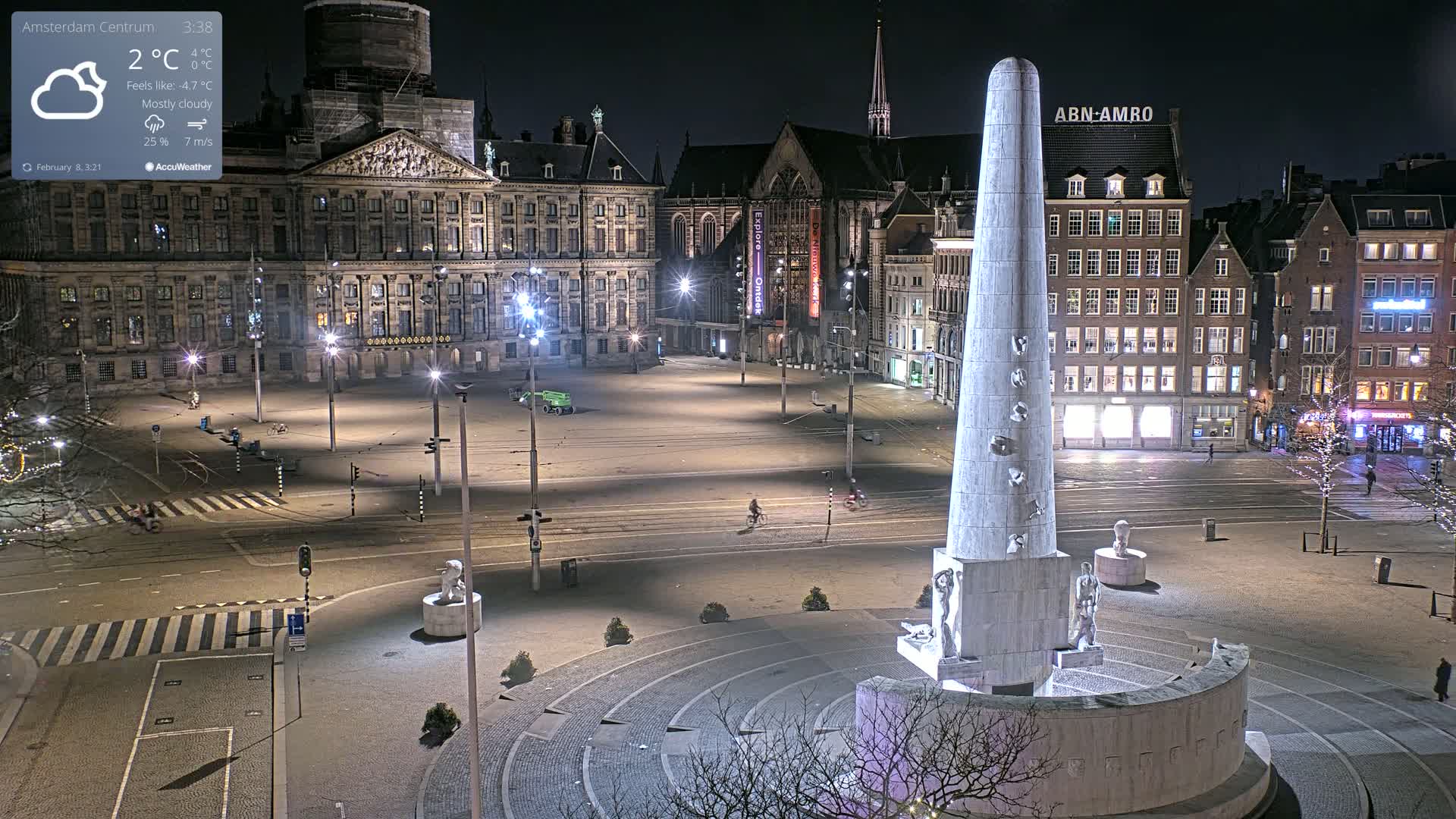 A mostly cloudy night scene shows a large, empty square in a European city, centered on a tall, light-colored obelisk monument surrounded by historical buildings and streetlights.