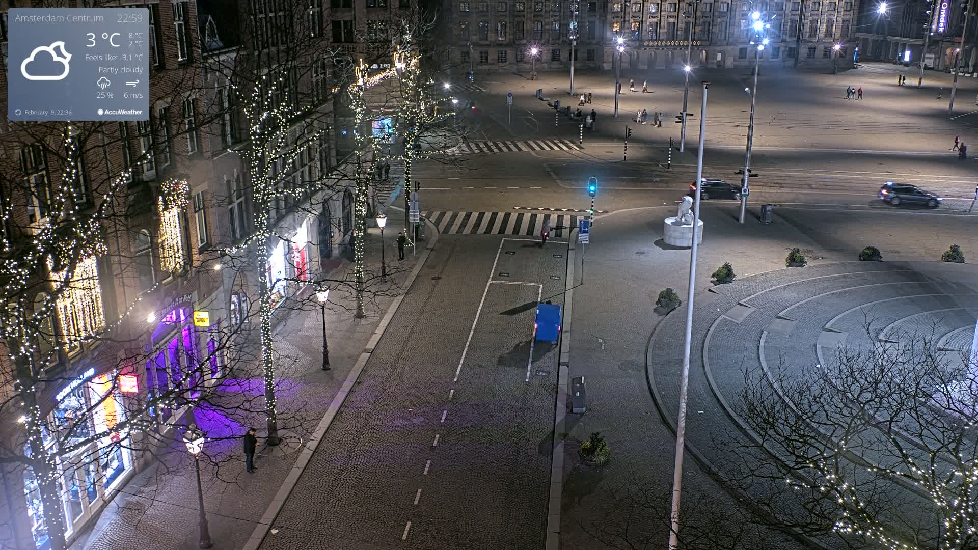 A nighttime, partly cloudy view of a city square and surrounding streets, decorated with Christmas lights on trees lining the sides of buildings.