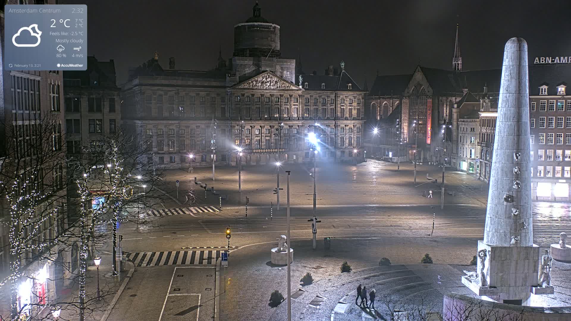 A mostly cloudy night scene shows a large, illuminated square in front of a palace, with a tall monument and several buildings surrounding the area.