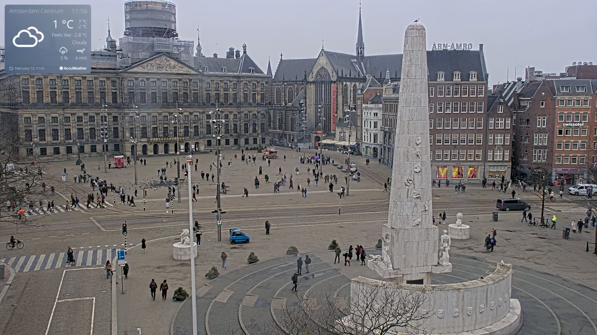 A cloudy, cool day in a large European city square, featuring a tall monument at the center, surrounded by pedestrians and historic buildings.
