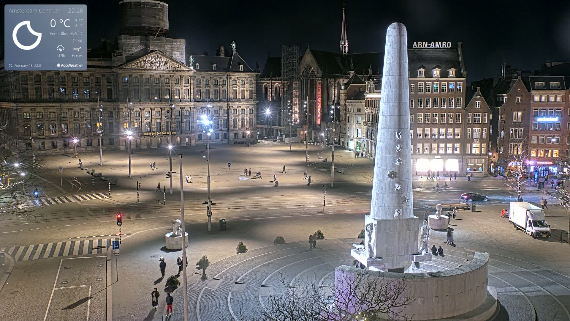 A nighttime view of a large, mostly empty square with a tall monument in the center, surrounded by buildings and illuminated by streetlights under a clear sky.