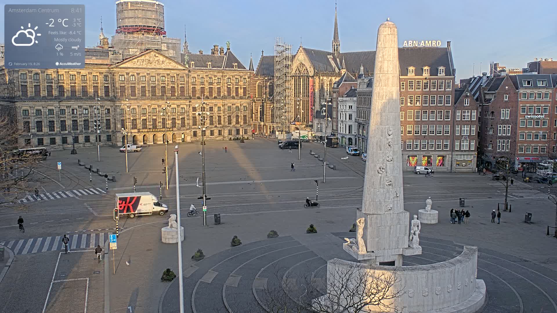 A mostly cloudy morning with a light breeze shows a large city square with a tall monument at its center, surrounded by historic buildings, including a palace and church, some of which are under construction.