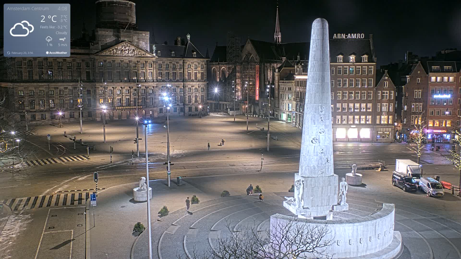 A nighttime, cloudy scene of a city square with a tall monument at its center, surrounded by historical buildings and sparsely populated by pedestrians.