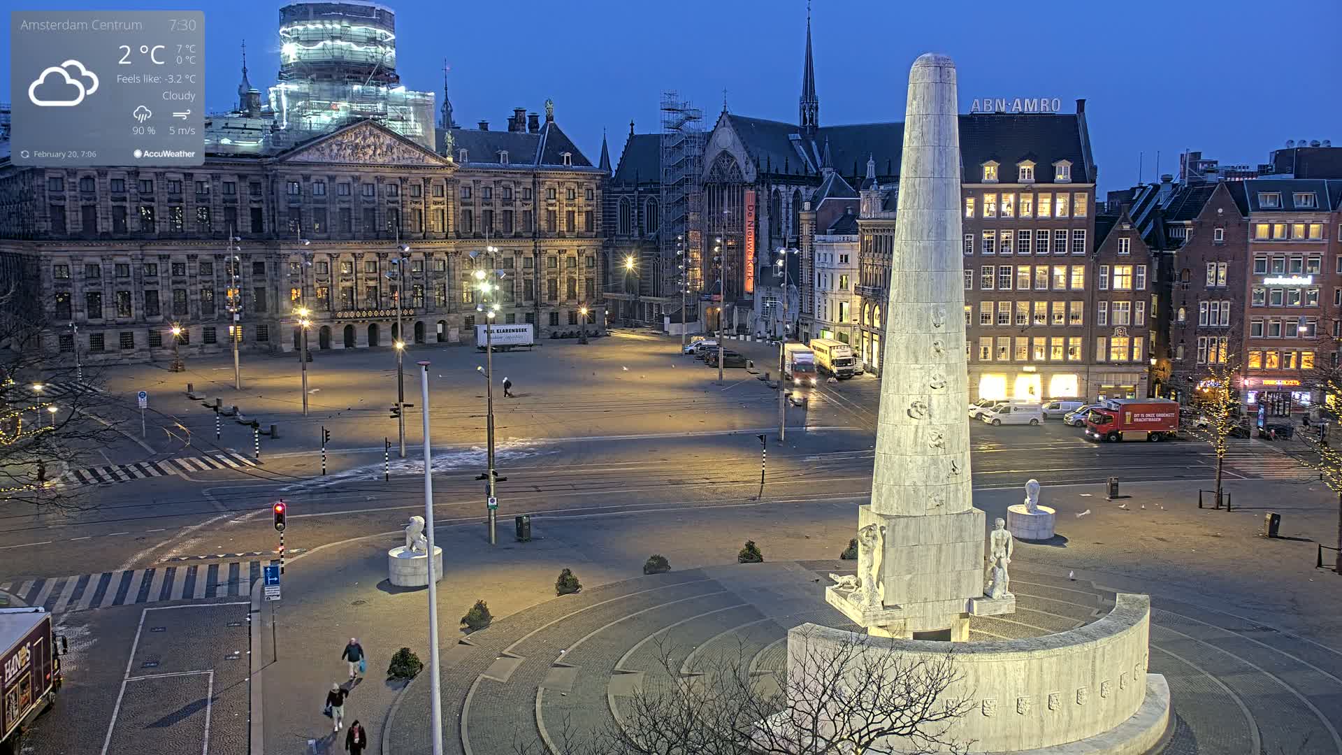 A large, mostly empty city square at twilight under cloudy skies, features a tall, obelisk-like monument in the foreground and historic buildings in the background.