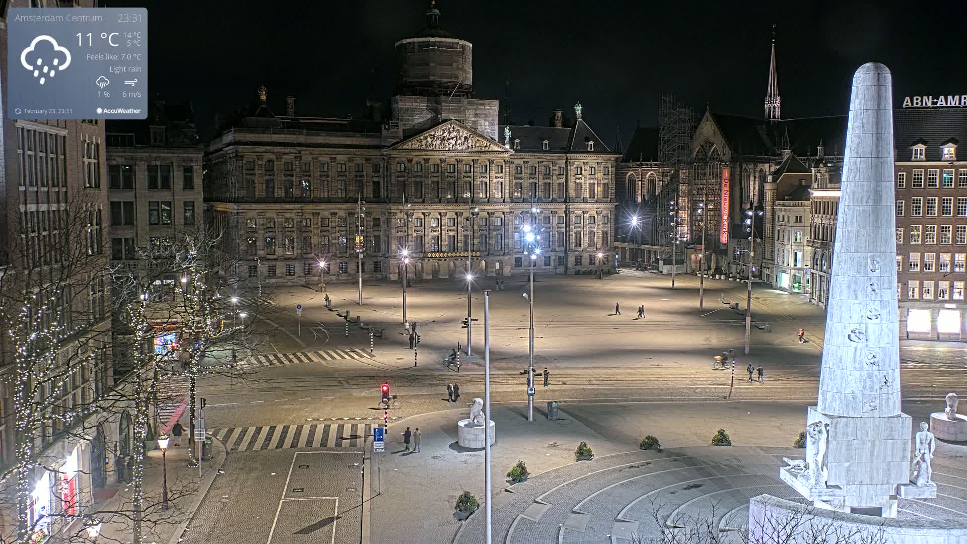 A nighttime, lightly raining view of a large, empty square in a European city, featuring a prominent palace, other buildings, and a tall, obelisk-like monument.
