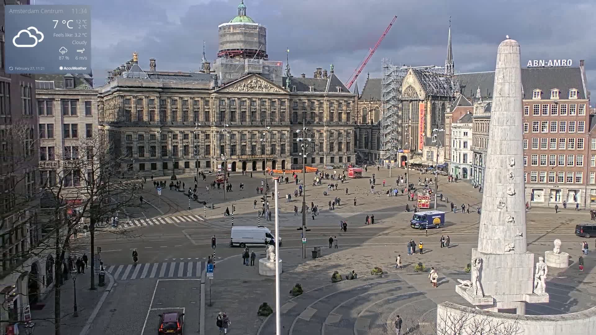 A cloudy, but sunny, day in a city square with a large palace, a monument, and several buildings surrounding it, with sparse pedestrian traffic.