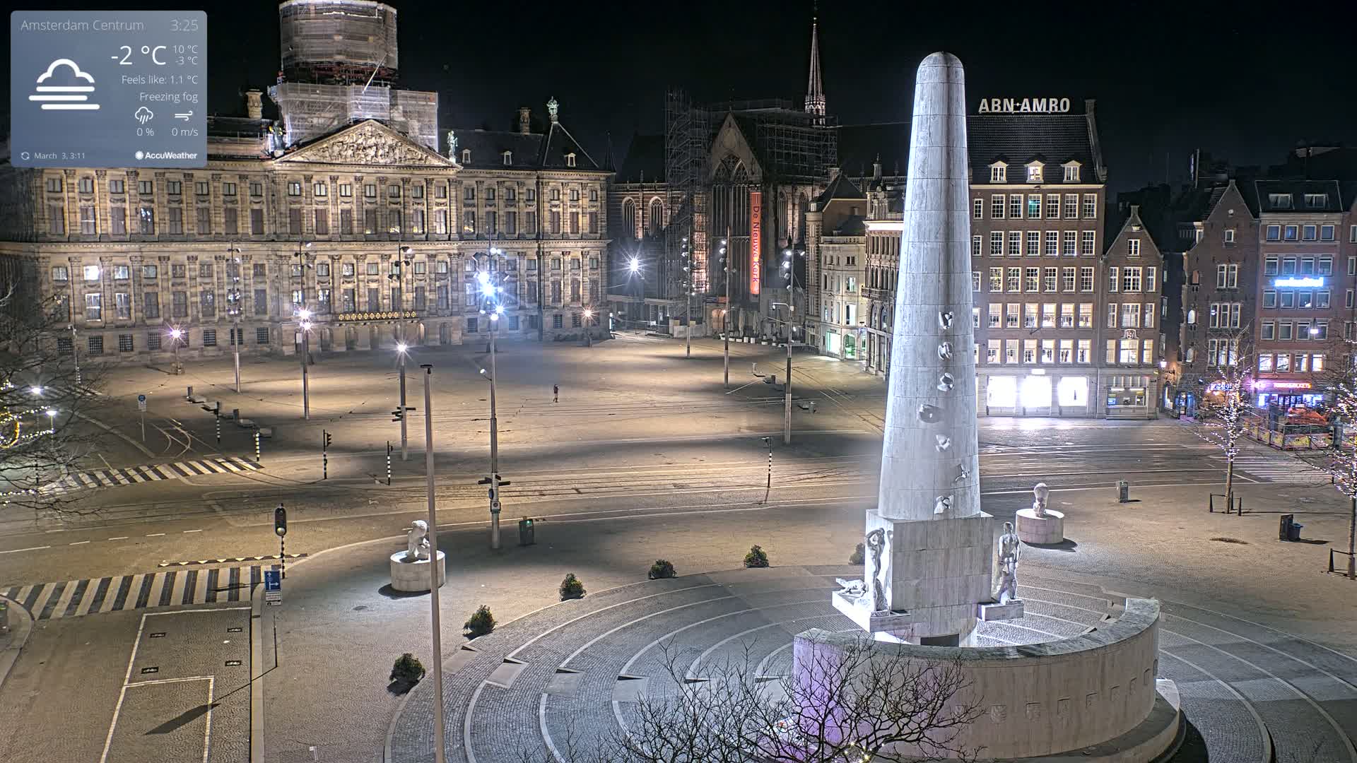 A nighttime, empty city square with a tall monument at its center, under freezing fog conditions.
