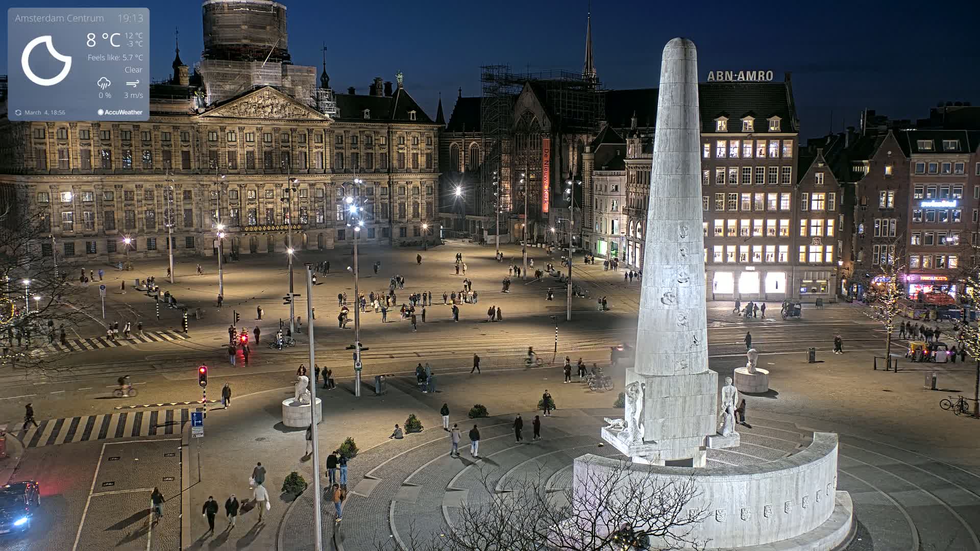 A nighttime view of a large city square with a tall monument in the center, surrounded by historic buildings under a clear sky.