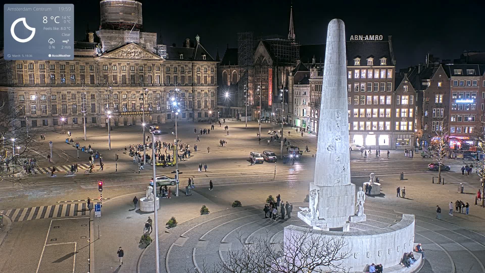 A nighttime view of a large, illuminated square with a tall monument at its center, surrounded by historic buildings under a clear sky.