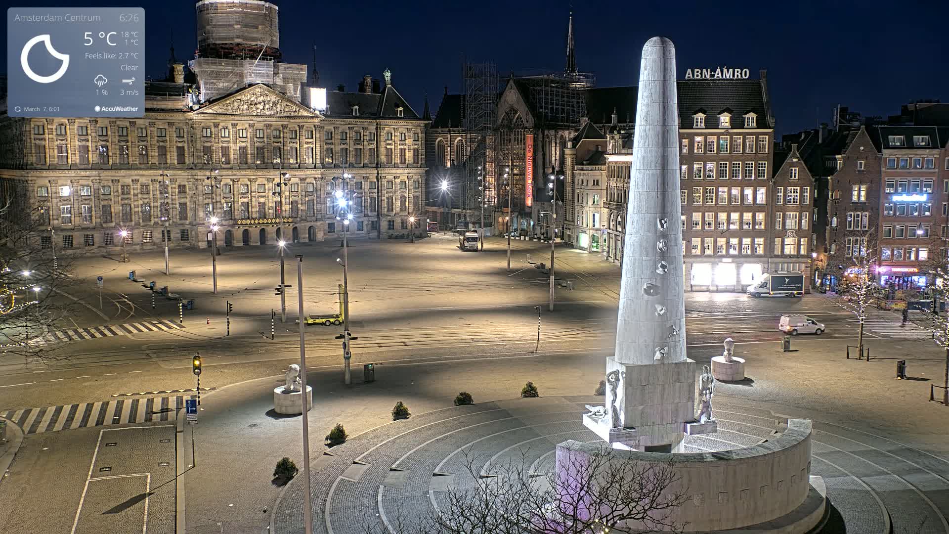 A mostly empty, illuminated plaza at night features a tall obelisk monument at its center, surrounded by classical-style buildings under a clear sky.