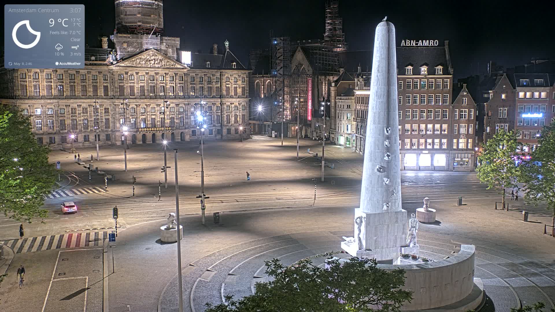 A nighttime view of a large, mostly empty square with a tall monument in the center, clear skies, and a large building in the background.