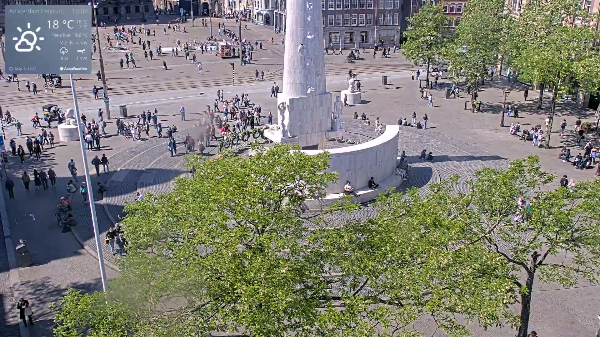 A mostly sunny square with a large monument in the center, surrounded by people and trees.