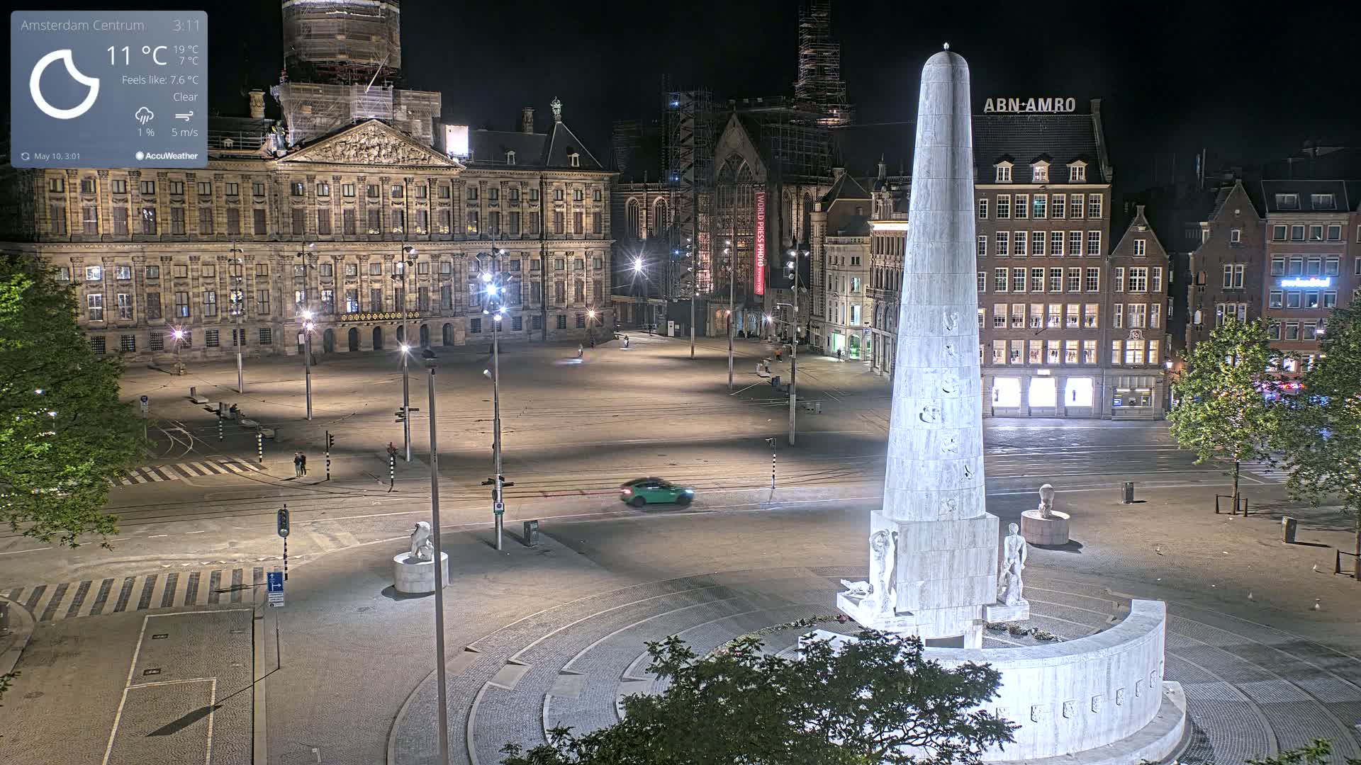 A nighttime, clear view of a city square with a tall obelisk monument at its center, surrounded by historic buildings, and a single car driving through.