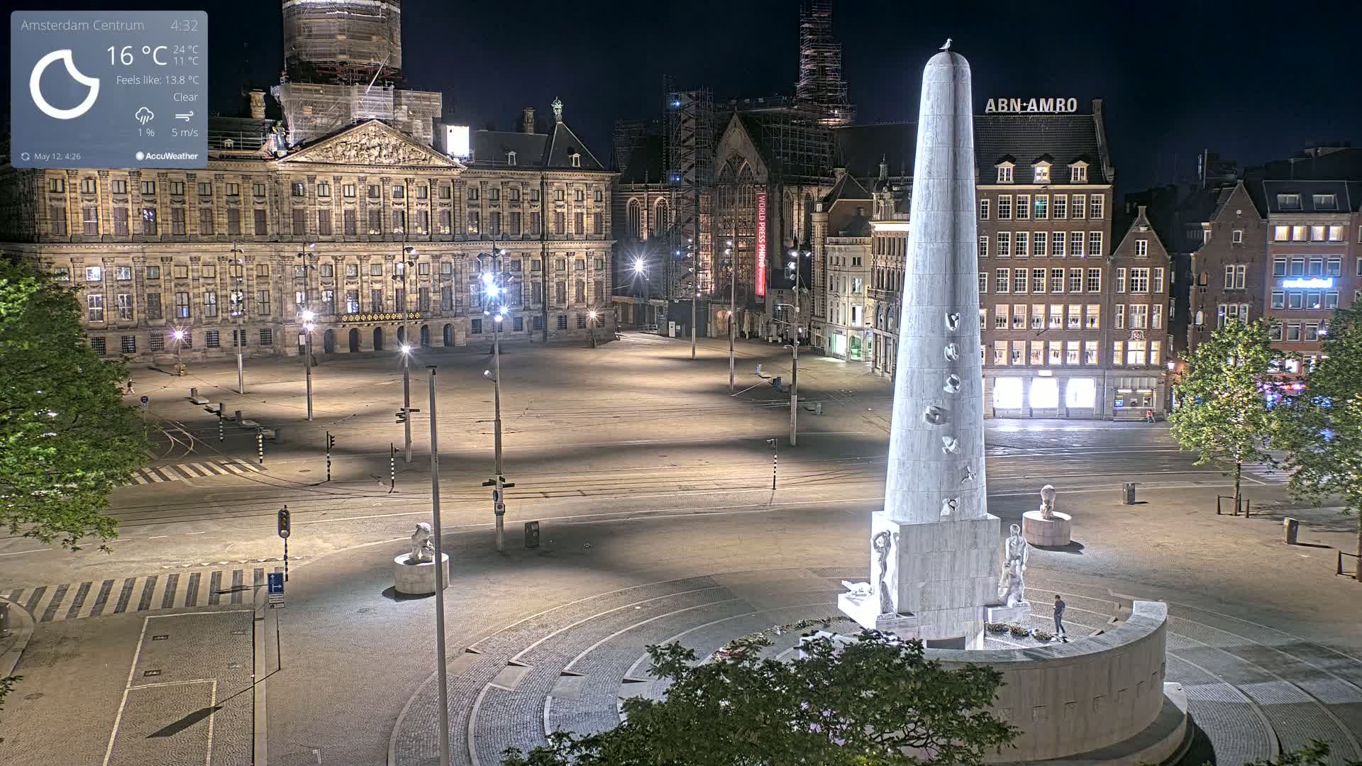A nighttime, clear view of a large, empty plaza with a tall, obelisk-like monument at its center, surrounded by historical-looking buildings.
