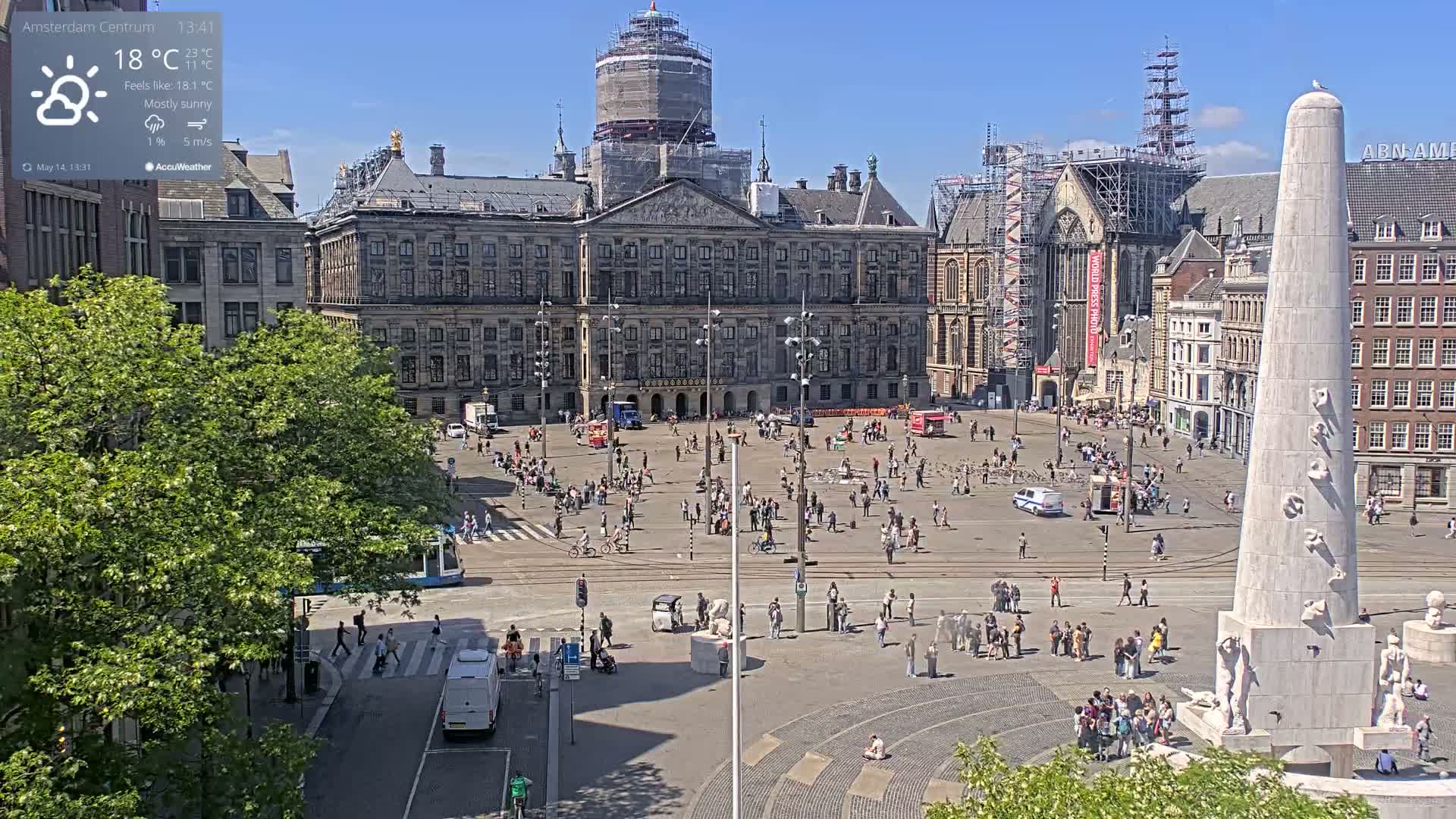 A mostly sunny city square, filled with people and featuring a large palace under construction and a tall obelisk-like monument.