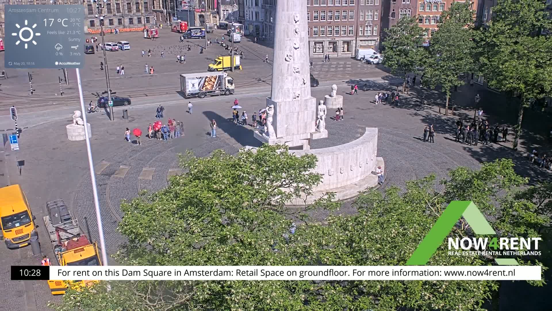 A sunny overhead view of Dam Square in Amsterdam, featuring a monument surrounded by people and greenery.