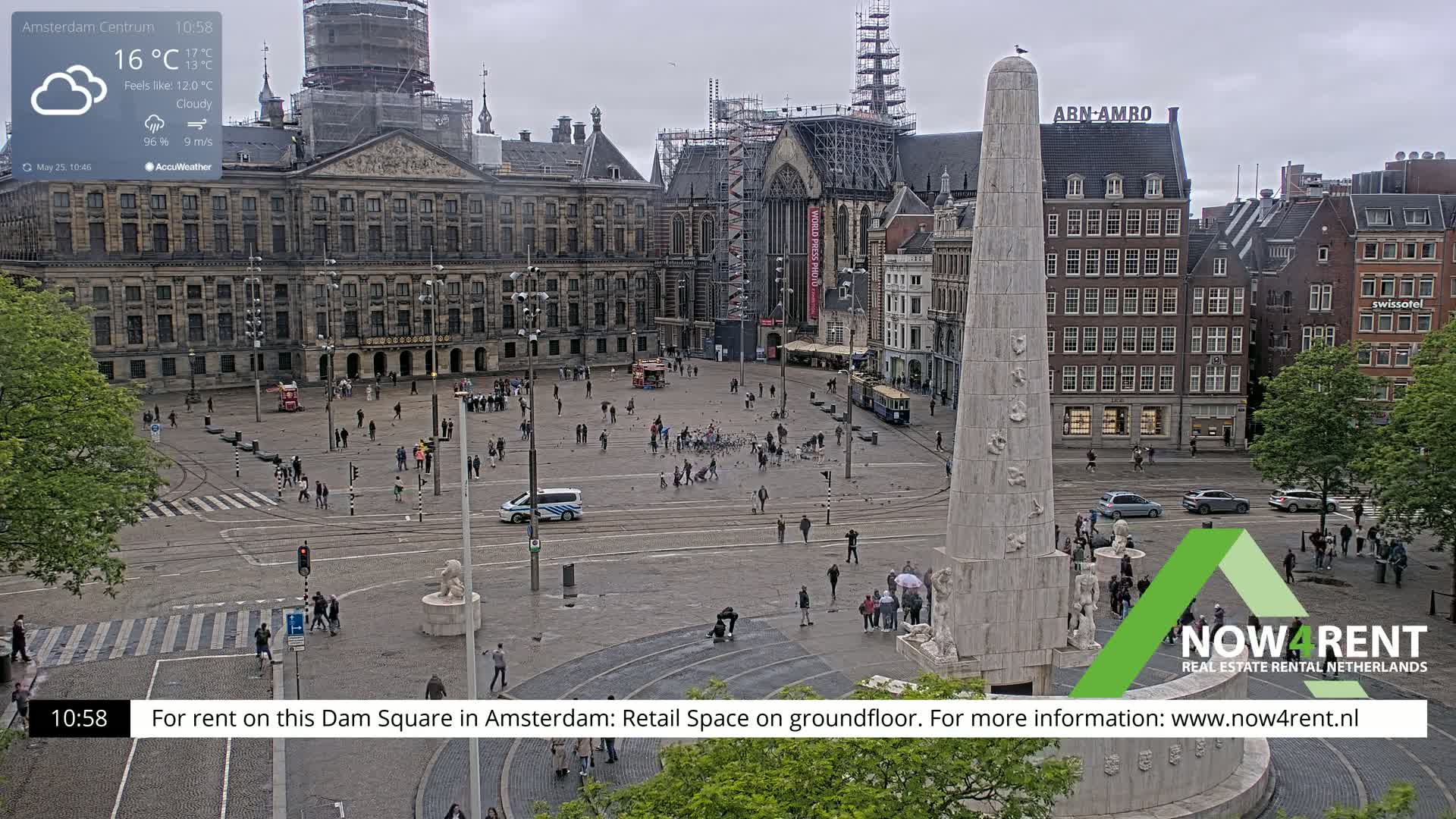A cloudy day in a large city square, featuring a tall monument and surrounding buildings, with several people walking around.