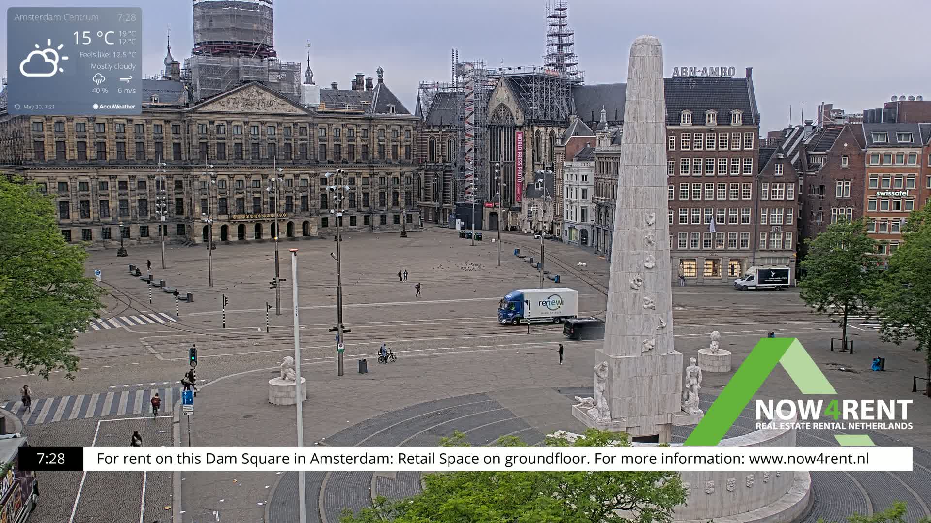 A mostly cloudy day in a large city square, featuring a monument, buildings under construction, and several vehicles.