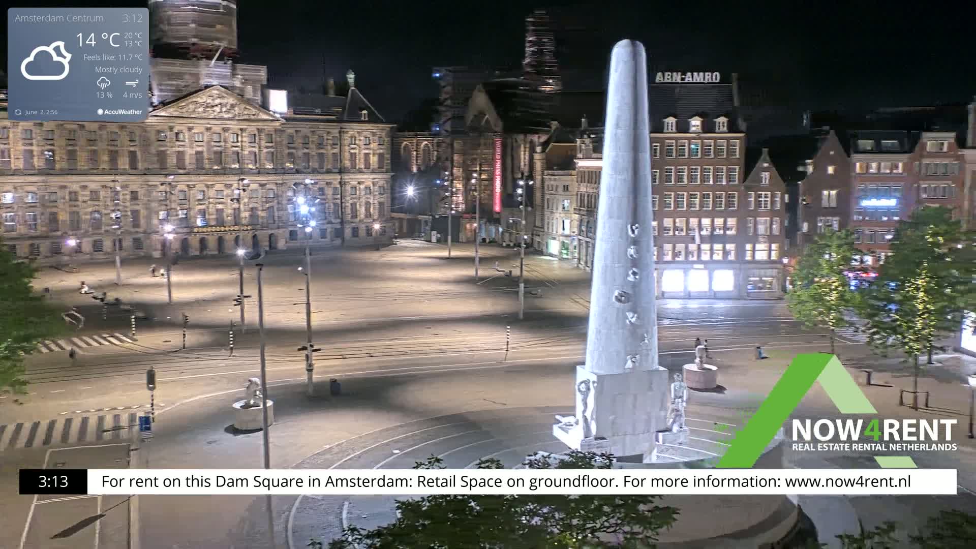 A mostly cloudy night scene shows a large, empty square in Amsterdam with a tall monument in the center, surrounded by historical buildings.