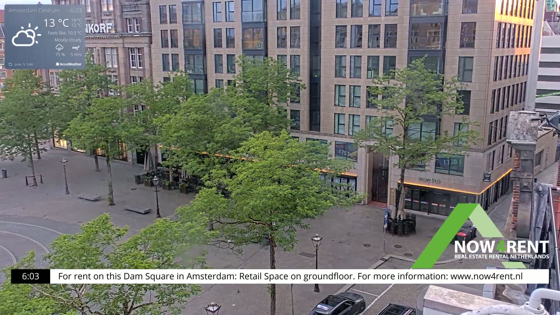 A mostly cloudy, 13°C day in a city square with several modern buildings and green trees.