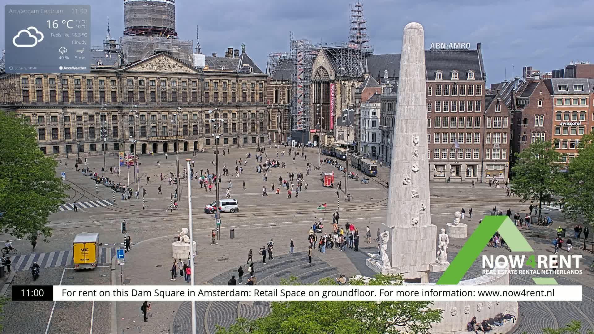 A cloudy day in a city square shows a large monument surrounded by people, buildings, and streetcars.