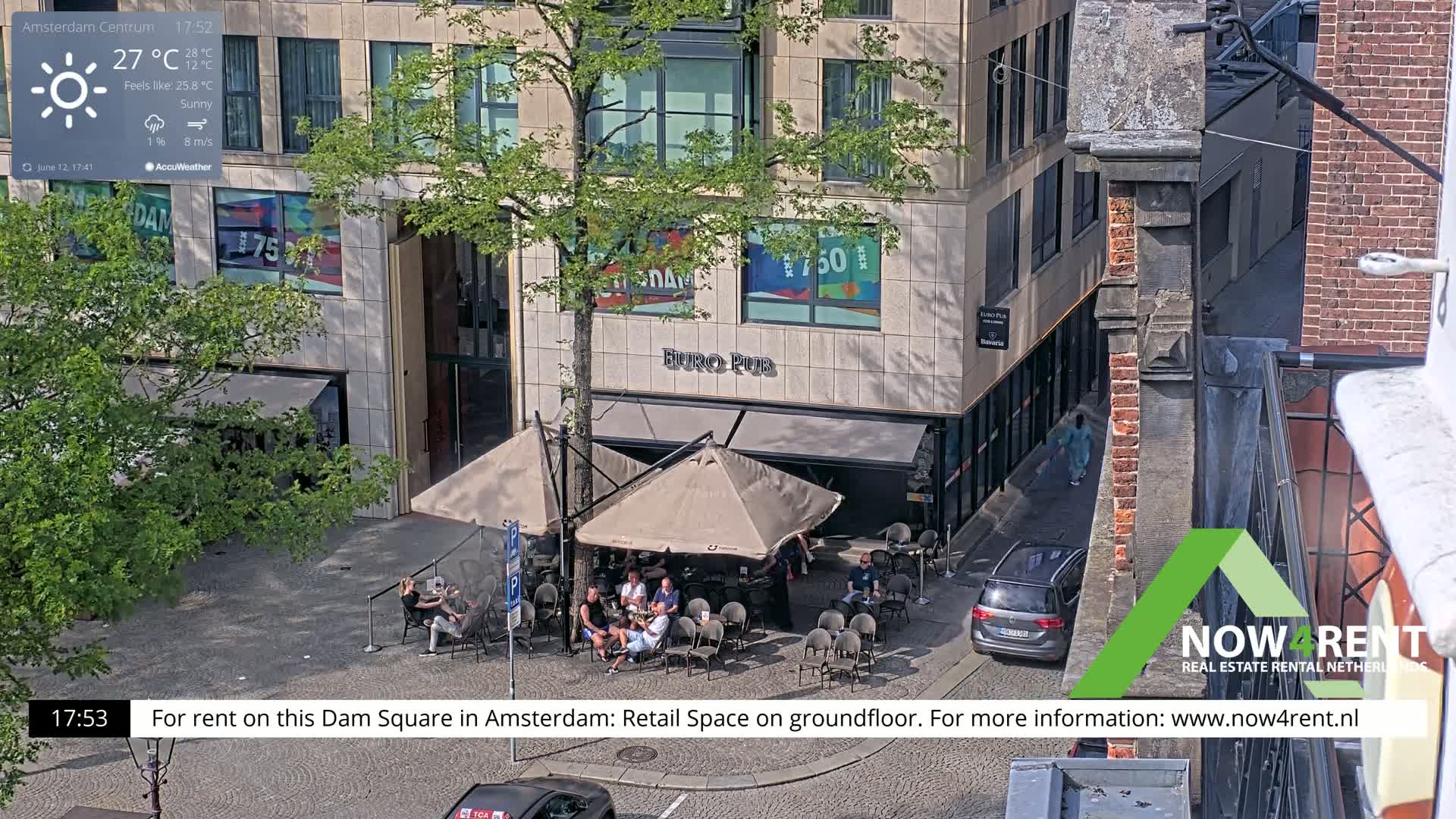 A sunny outdoor scene shows a Euro Pub patio with several people seated at tables under umbrellas, situated near a street with a car parked, all adjacent to a multi-story building.