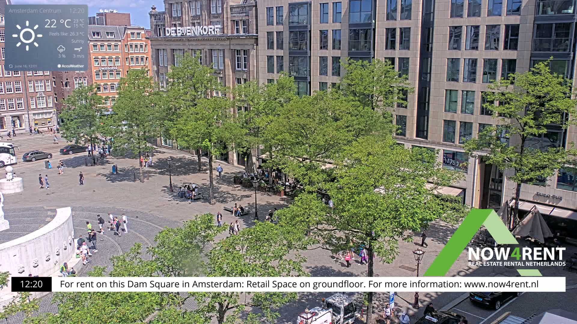 A sunny Dam Square in Amsterdam shows people walking among trees and buildings, with a partially visible fountain in the foreground.