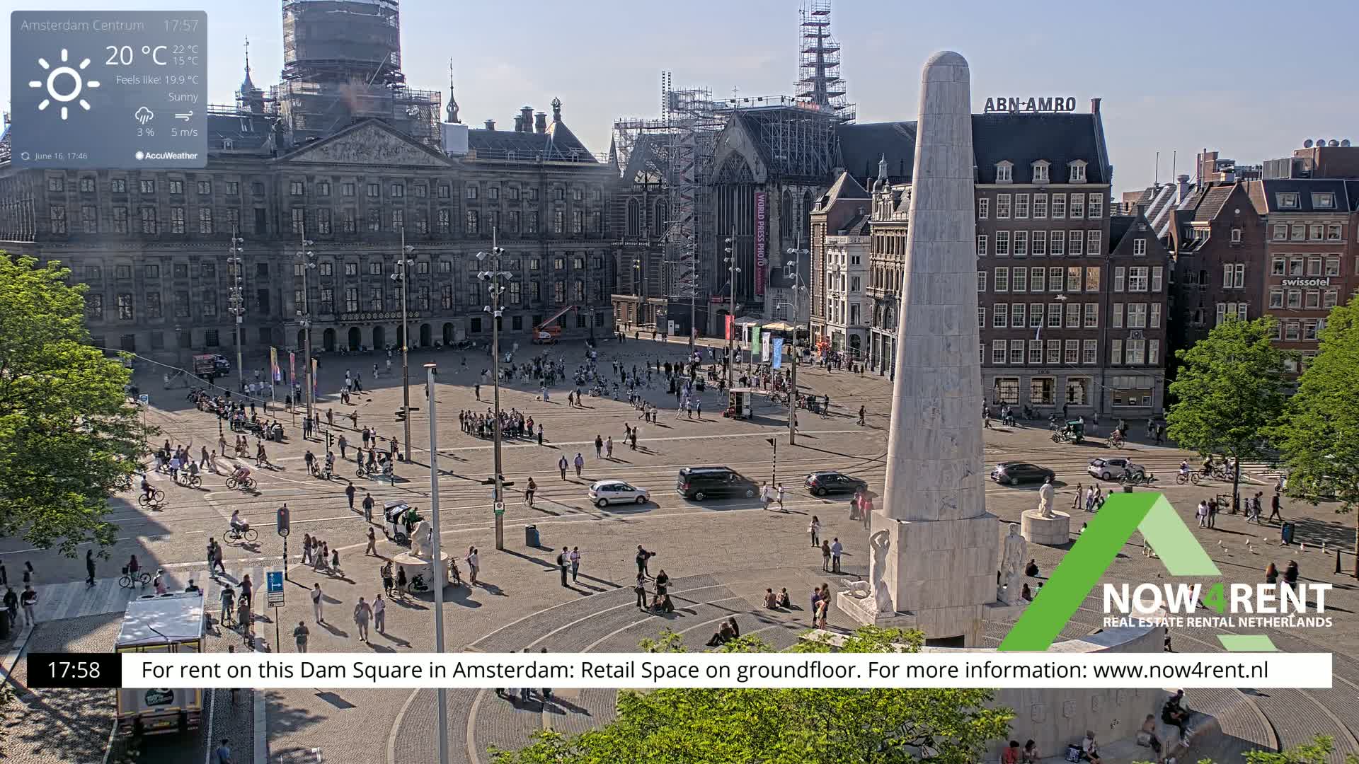 A sunny, crowded Dam Square in Amsterdam features a large monument, surrounding buildings, and tram lines.