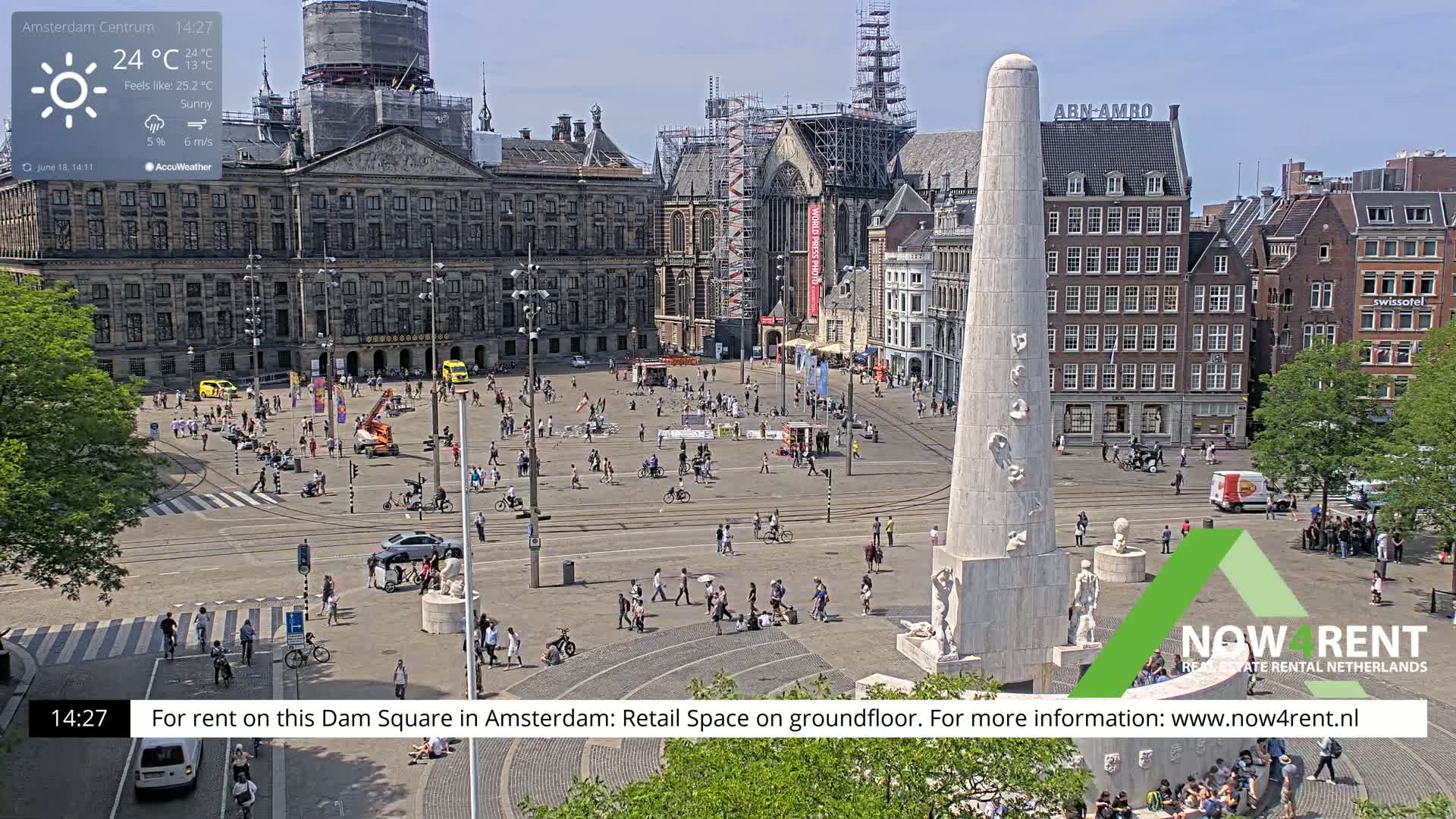 A sunny Dam Square in Amsterdam, with a monument at the center, is filled with pedestrians and vehicles on a partly cloudy day.