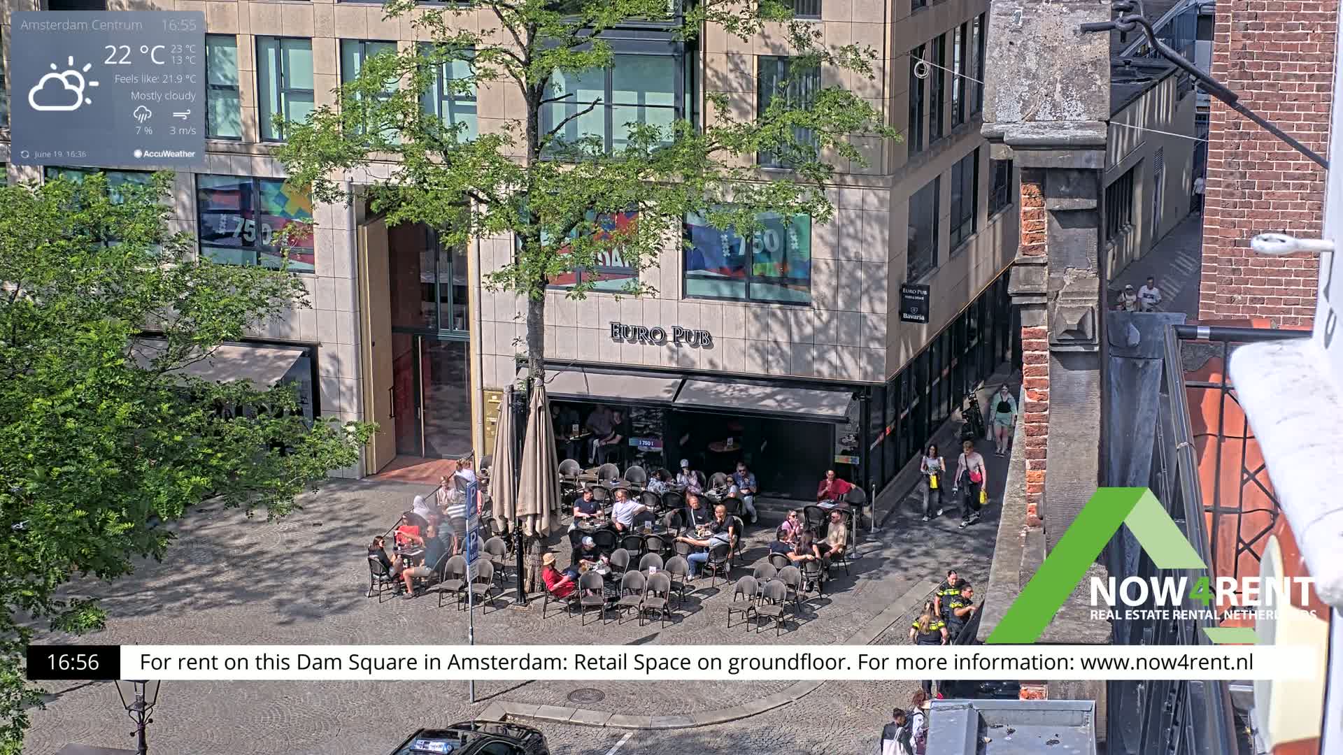 A mostly cloudy outdoor scene shows a Euro Pub with patrons seated at tables in a city square, with people walking by on the sidewalk.