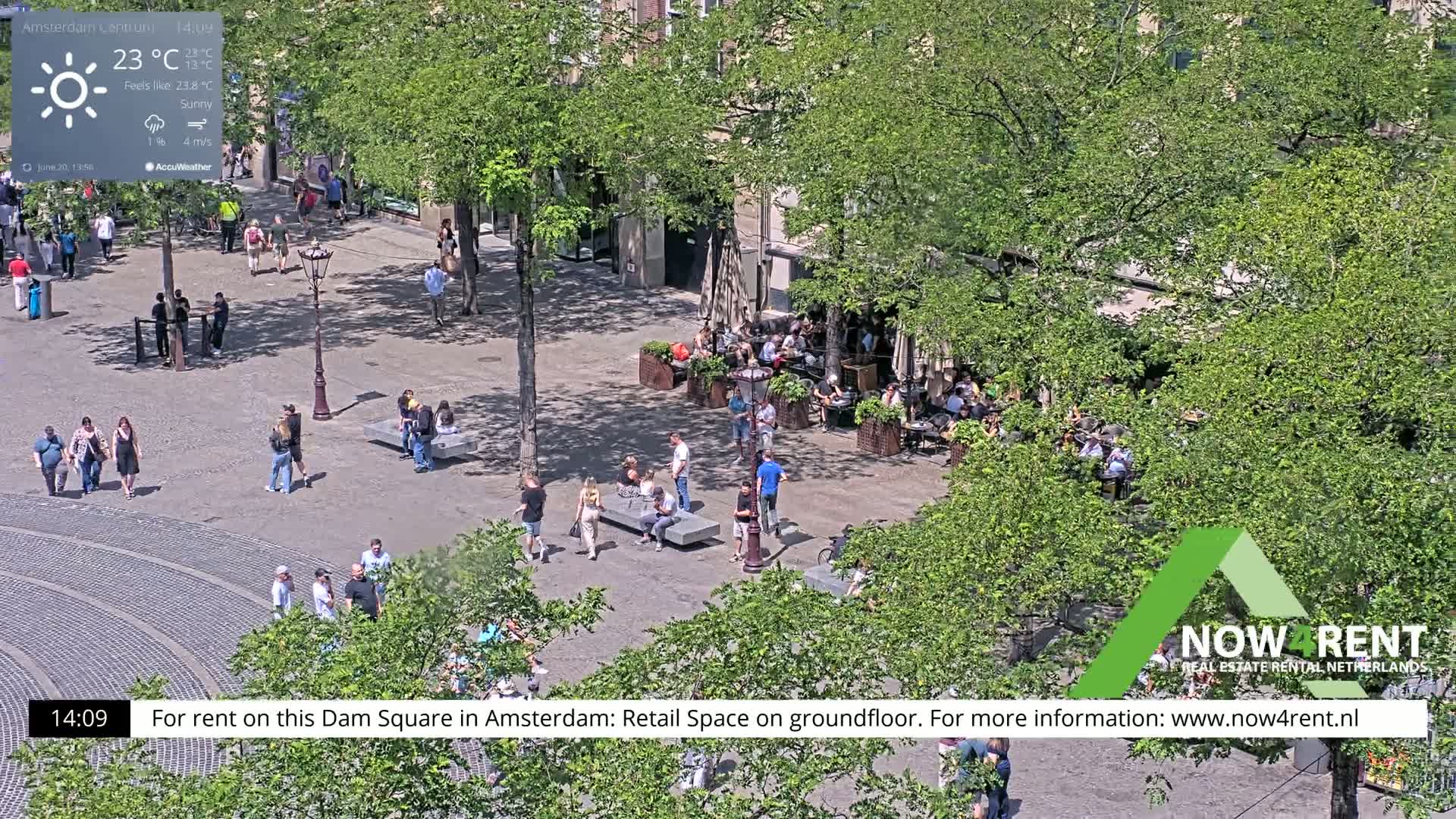 A sunny Dam Square in Amsterdam shows people walking and sitting at outdoor cafes under leafy trees.