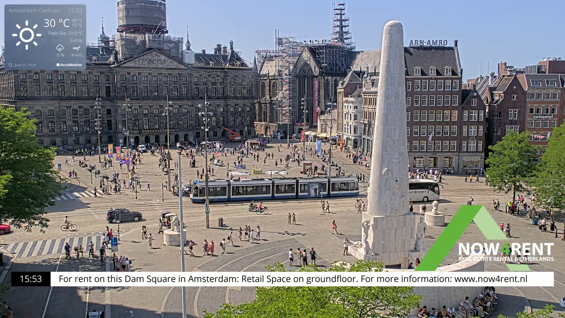 A sunny Dam Square in Amsterdam shows a tram, many pedestrians, and a large monument, with buildings under construction in the background.