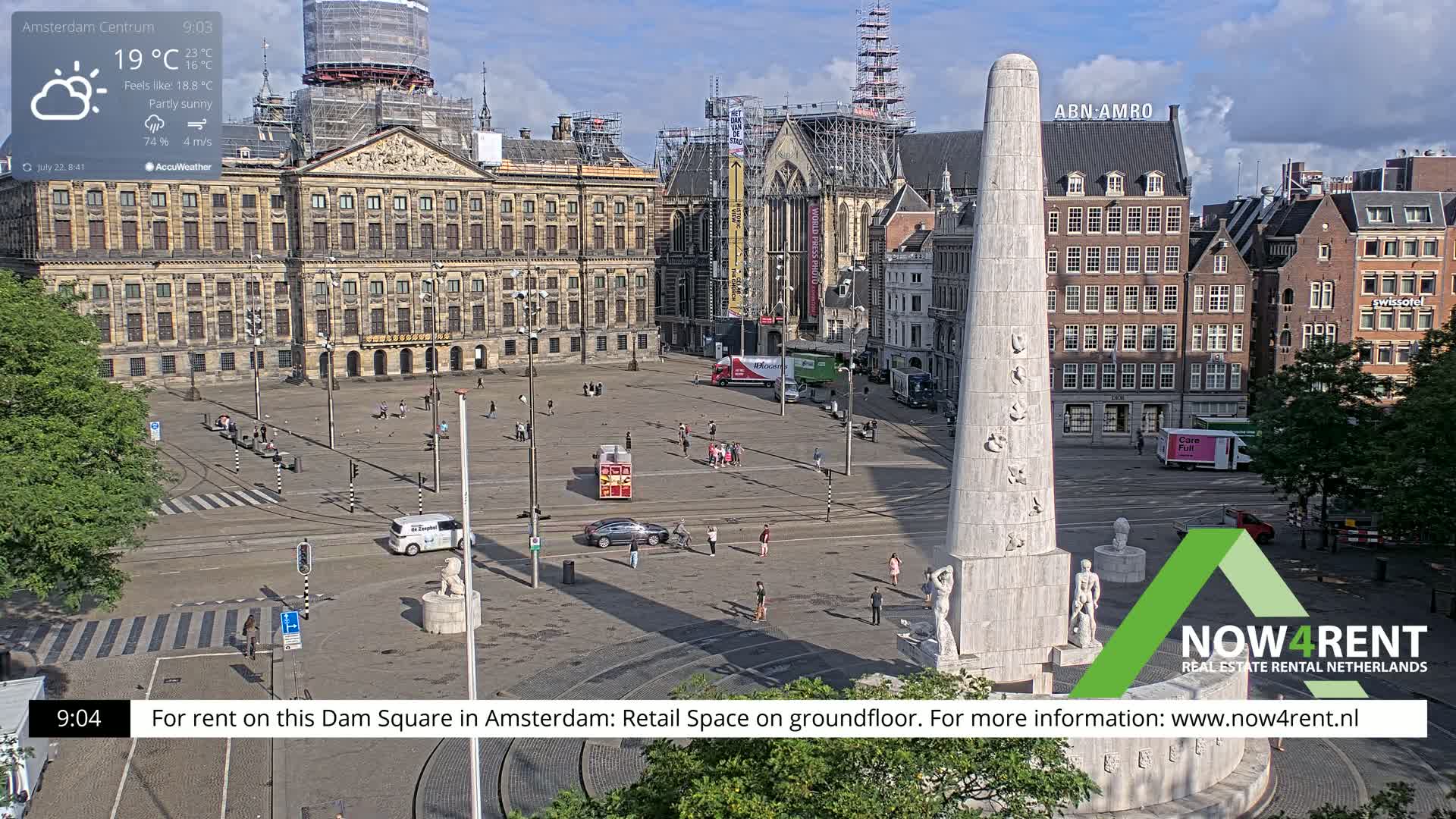 A partly sunny Dam Square in Amsterdam features a large monument, surrounding buildings, and a few people scattered throughout the plaza.