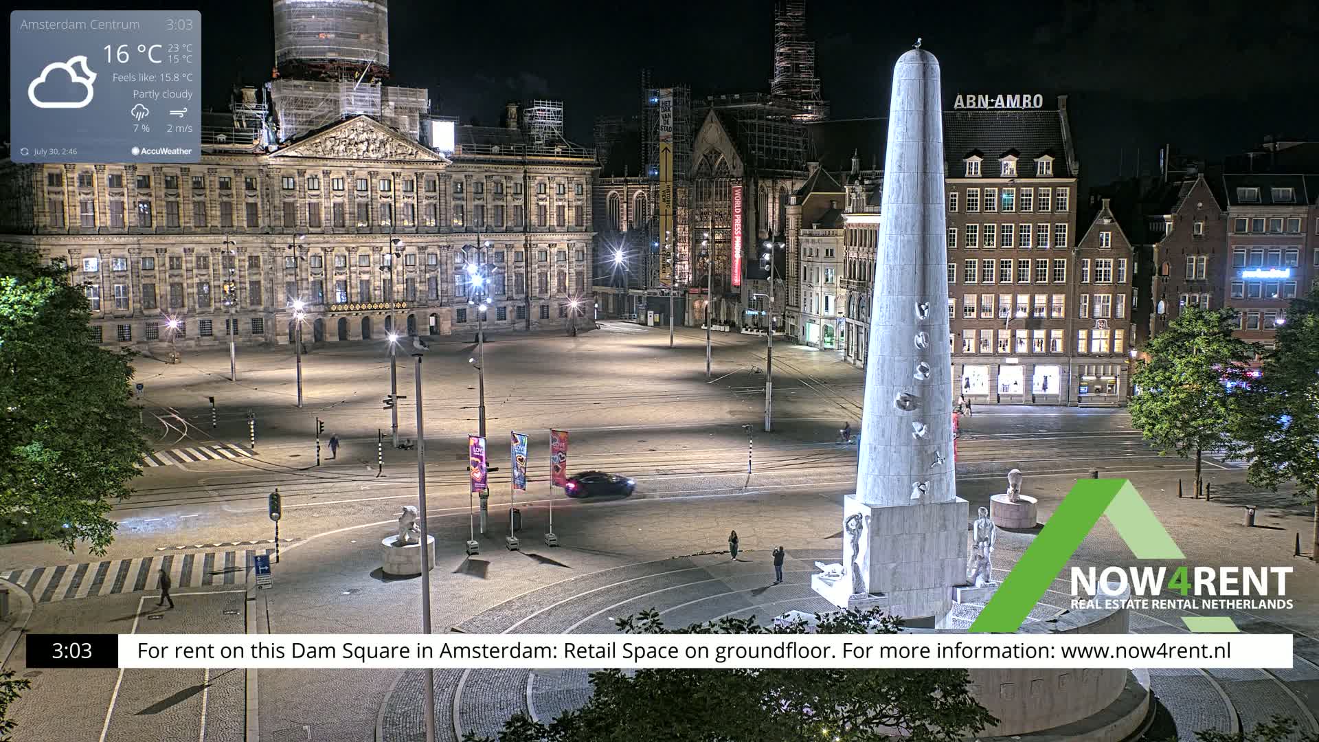A partly sunny Dam Square in Amsterdam features a large monument, surrounding buildings, and a few people scattered throughout the plaza.