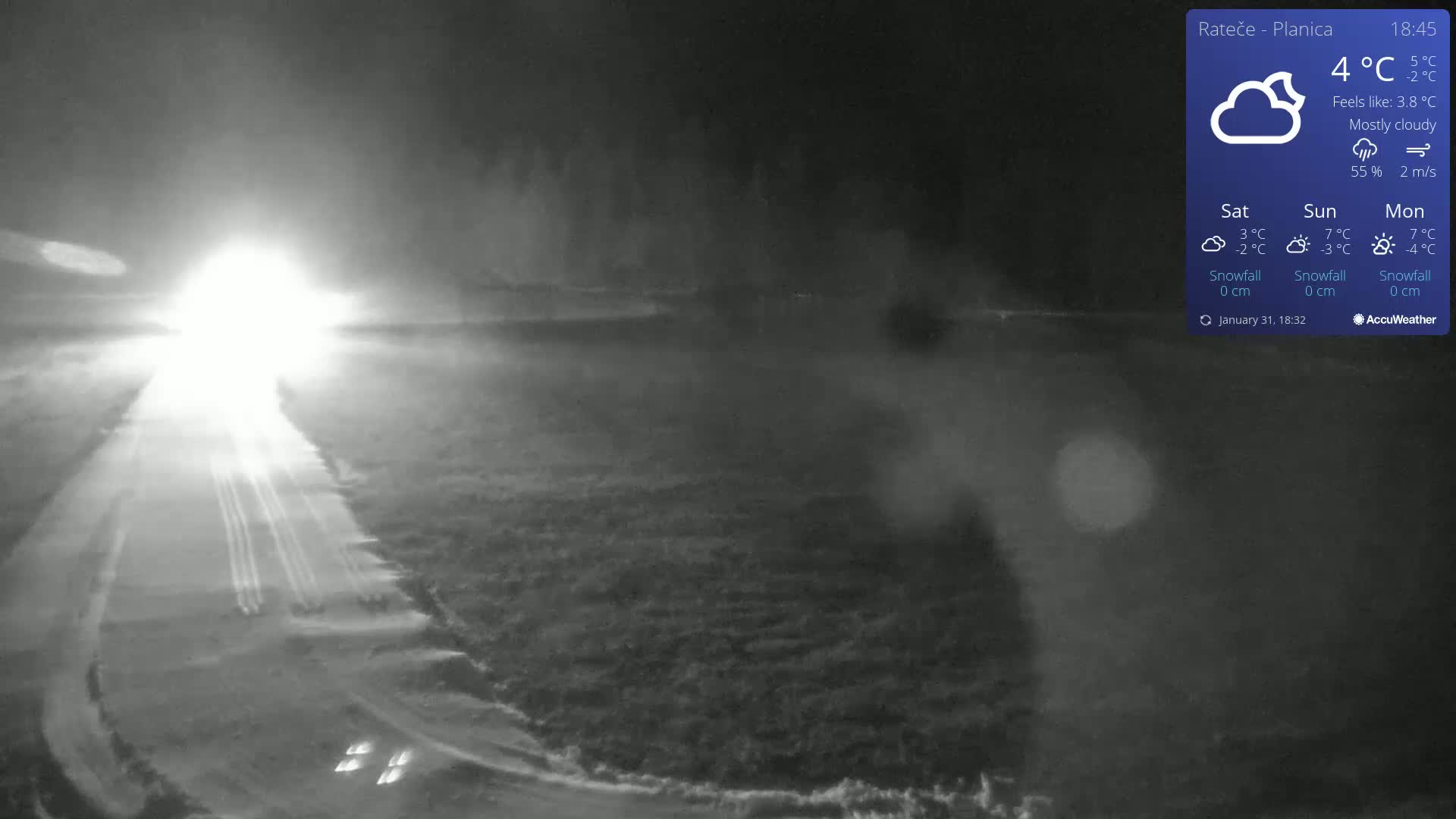 A nighttime, mostly cloudy scene shows a road with headlights approaching, and the surrounding landscape is dimly lit.