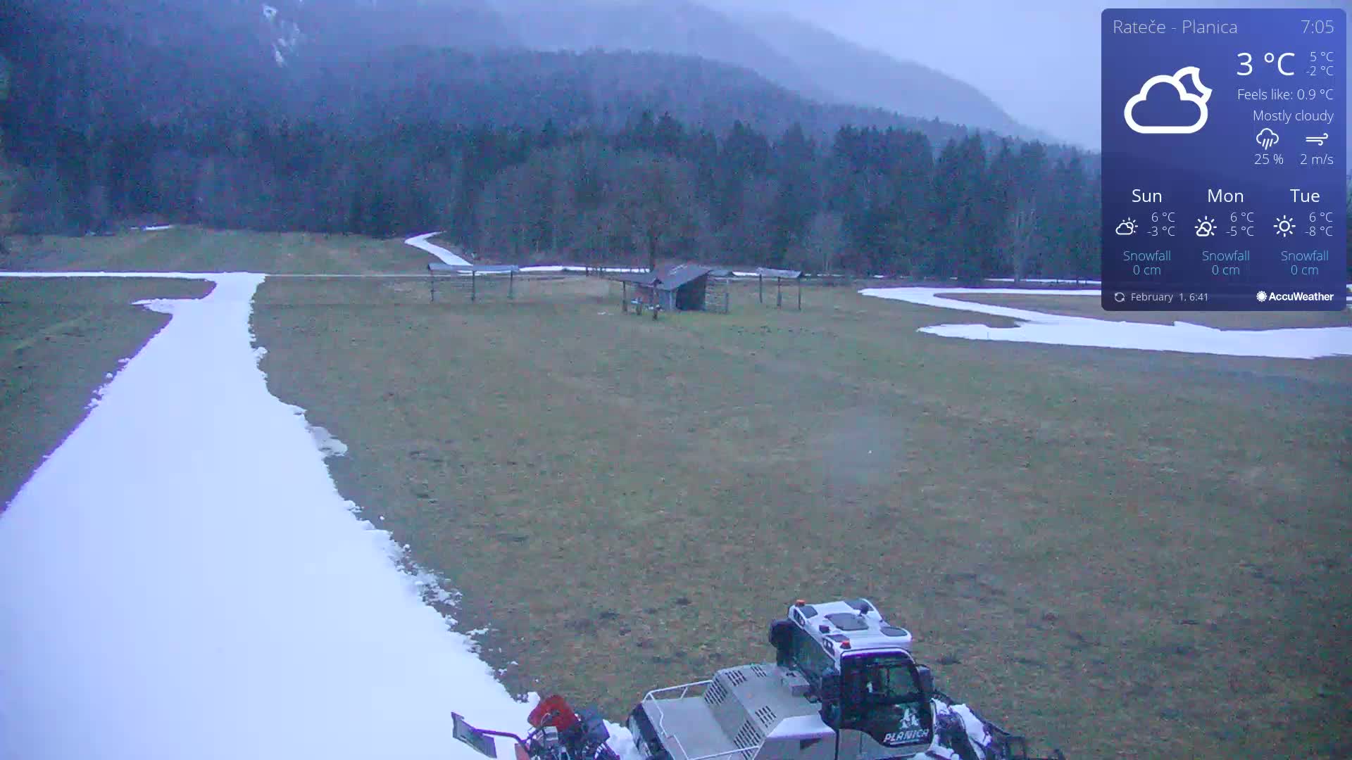 A snowcat is parked on a mostly brown field with a thin, winding path of snow, under a mostly cloudy sky.