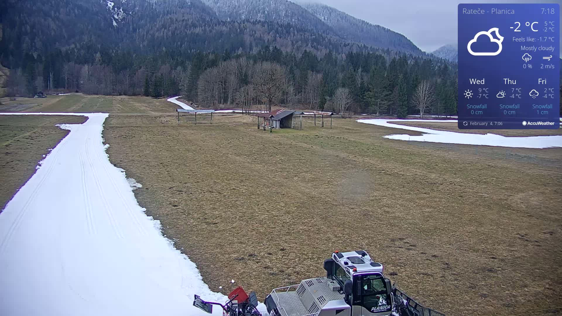 A snow groomer is preparing a snow-covered cross-country ski trail in a mostly cloudy, cold outdoor setting with a mountain backdrop.