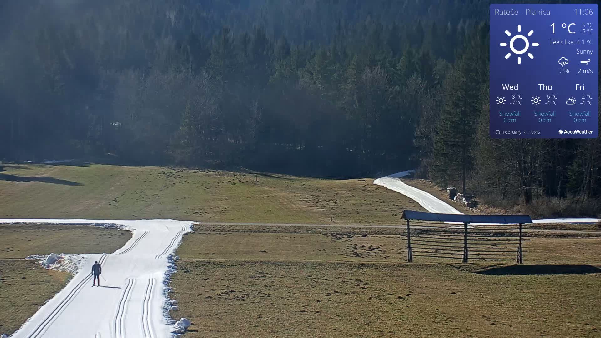 A cross-country skier is seen on a snow-covered track in a sunny, open field bordered by a dark forest.