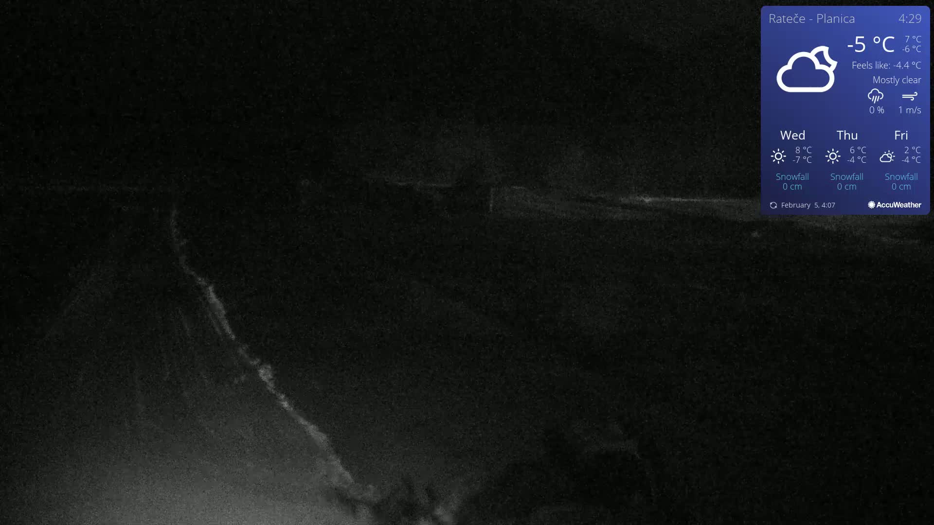A mostly clear, dark nighttime scene shows a dimly lit, snow-covered landscape with a faint, bright streak in the lower left.