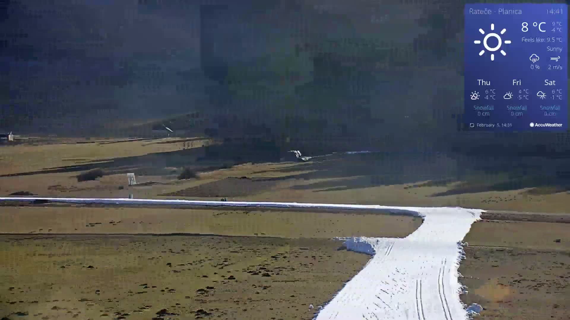 A sunny, snow-covered ski slope winds through a mostly barren, brown landscape under a clear sky.