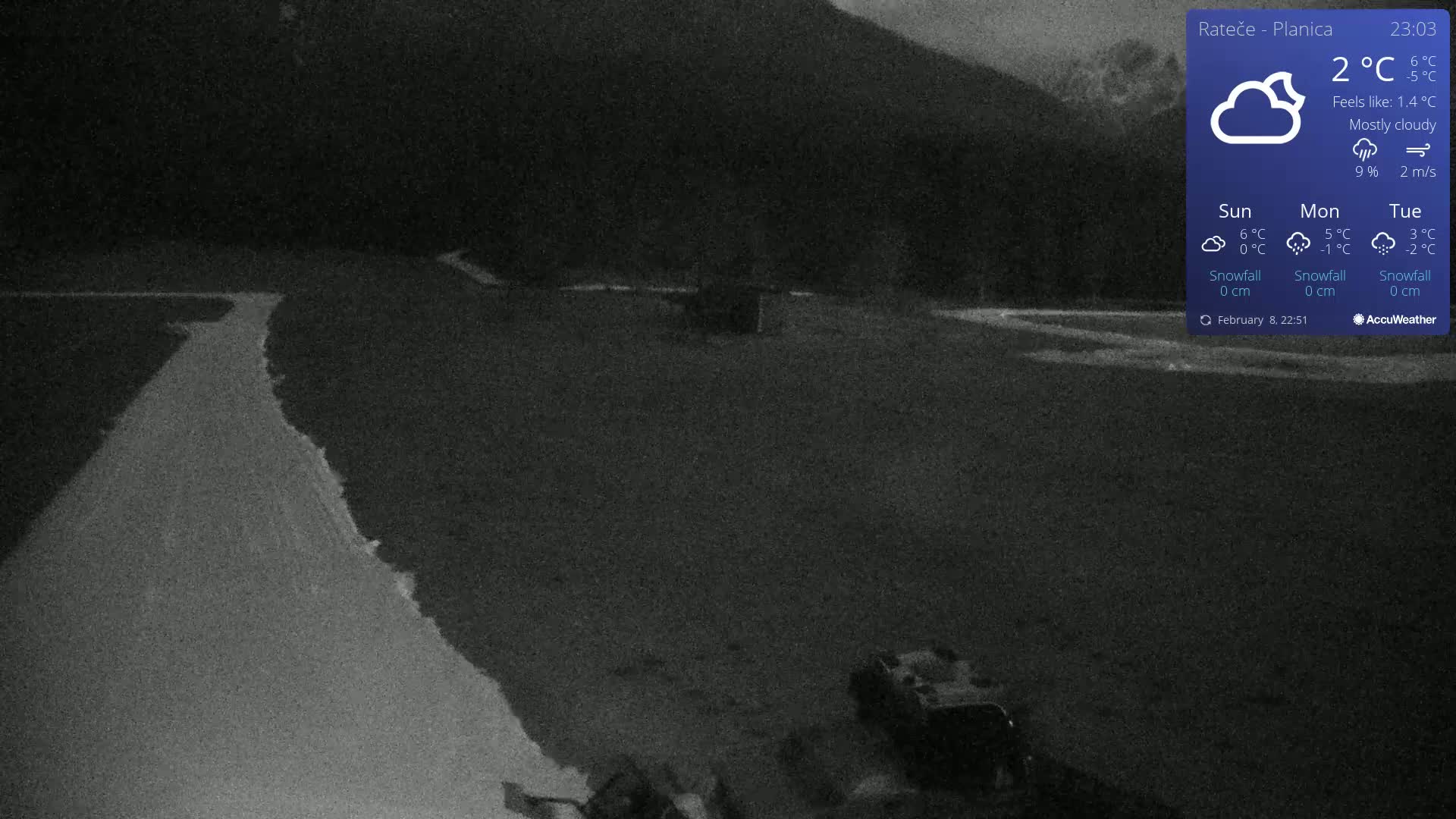 A mostly cloudy night scene shows a dark road curving through a flat, dark area with a vehicle in the lower right corner under a dark mountain.