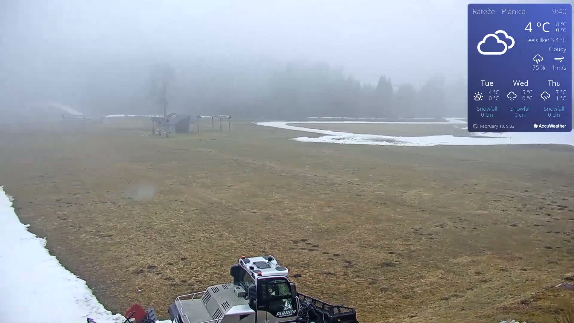A snowcat sits in a foggy field near a partially snow-covered clearing and wooded area.