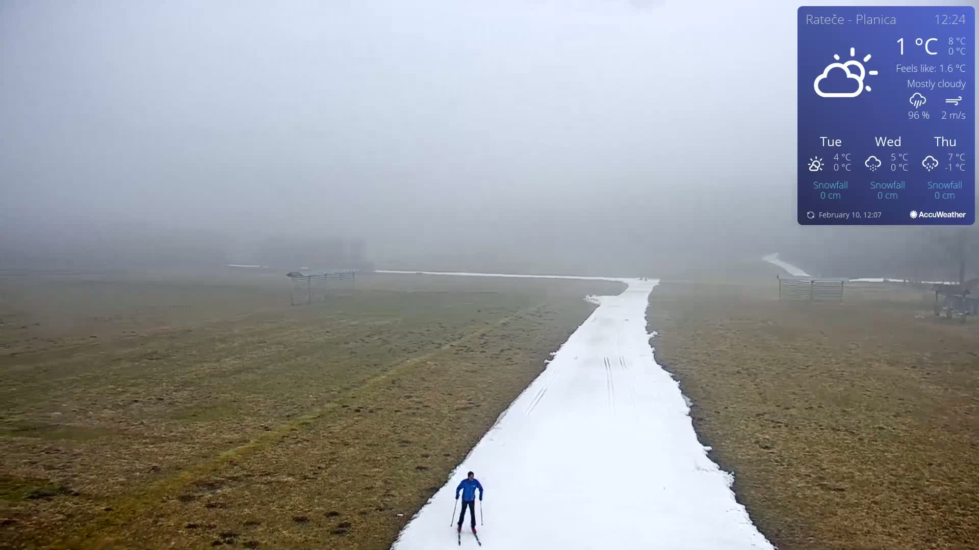 A cross-country skier traverses a snow-covered path amidst a foggy, mostly cloudy landscape.