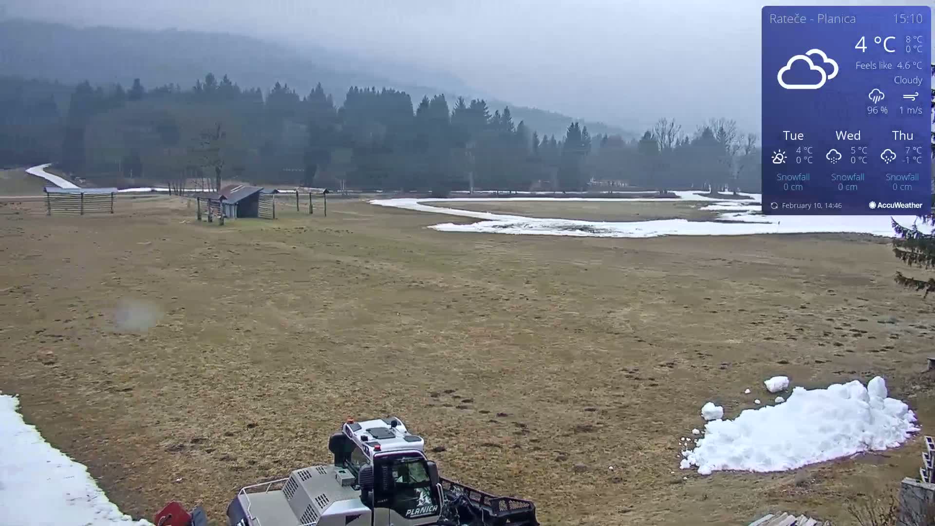 A snowcat is parked on a mostly brown field with patches of snow, under a cloudy sky.