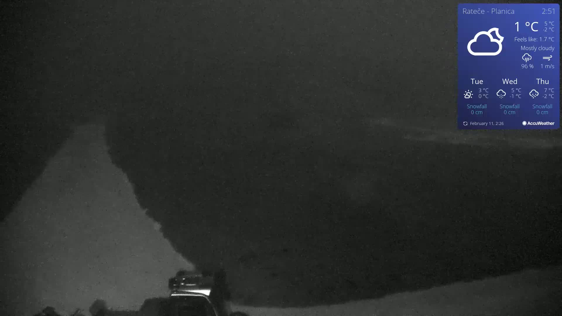 A nighttime, mostly cloudy scene shows a dark, snow-covered landscape with a vehicle partially visible in the lower left corner.