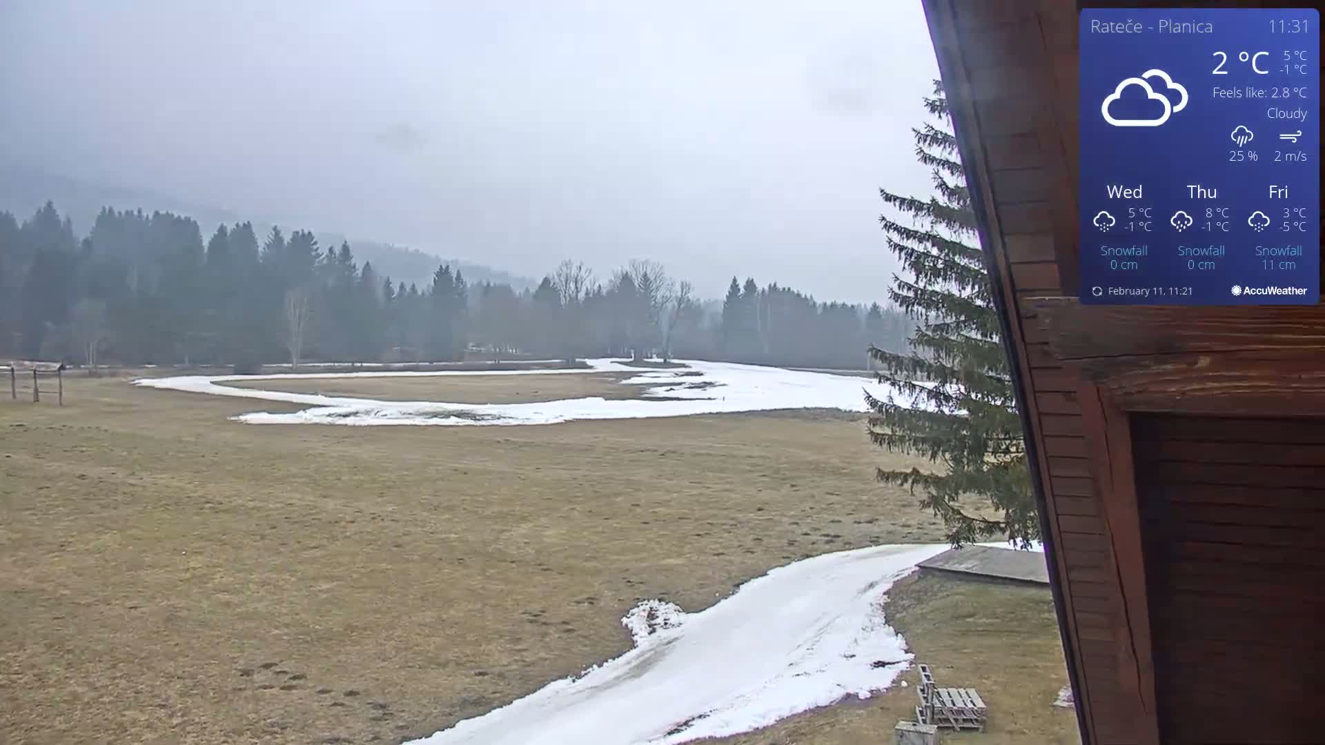 A partially snow-covered field with a winding path and a line of trees in the background under cloudy skies.