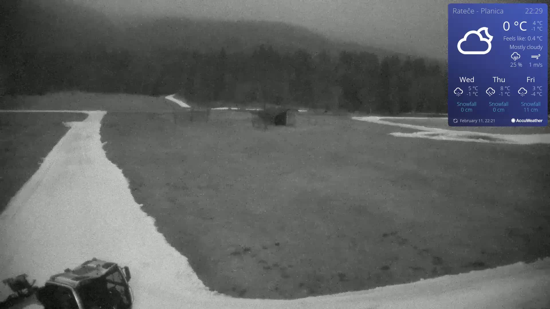 A mostly cloudy, dark scene shows a snow-covered field with a winding, lighter-colored path, a piece of machinery at the bottom left, and a dark forest in the background.