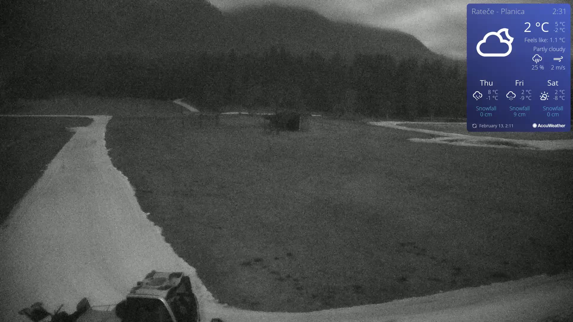 A partly cloudy, dark scene shows a snow-covered, flat, open area with a road and a machine in the bottom left corner, mountains are visible in the background.